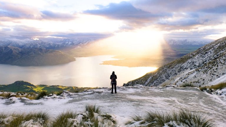 A hiker soaks in a dramatic sunrise on a snowy Roy's Peak trail over Lake Wanaka in New Zeland.