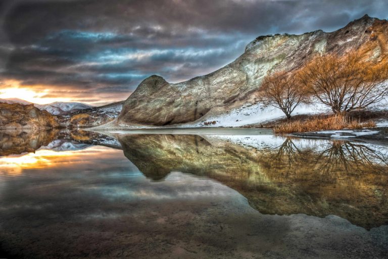 Blue Lake reflections of clay cliffs at sunset, after winter storm and snowfall, St Bathans, Central Otago, New Zealand