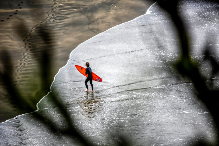 Surfer standing at Piha Beach, New Zealand