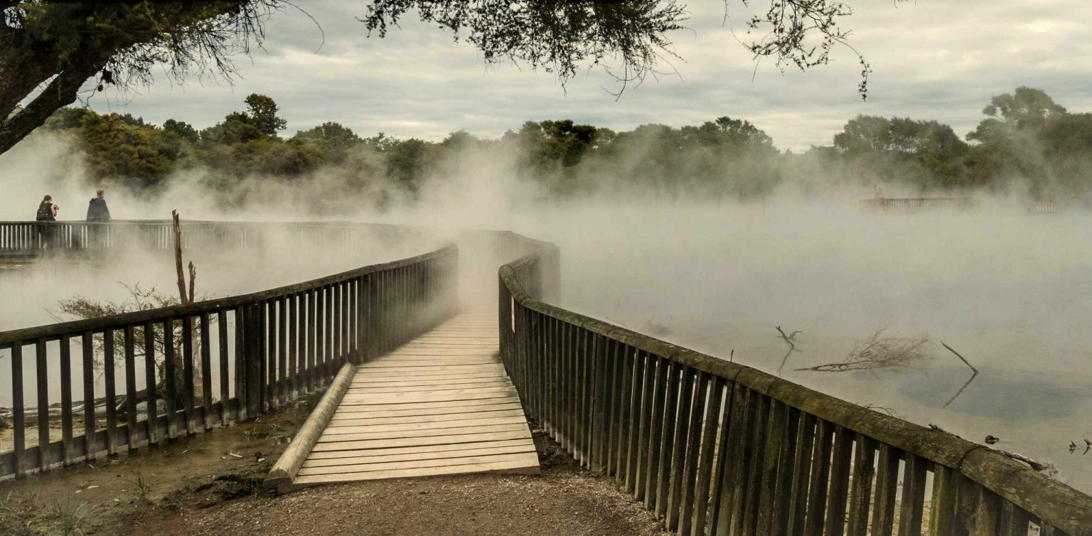 Wooden pathway leading through boiling lake and surrounded by steam. Shot in Kuirau Park in Rotorua, New Zealand