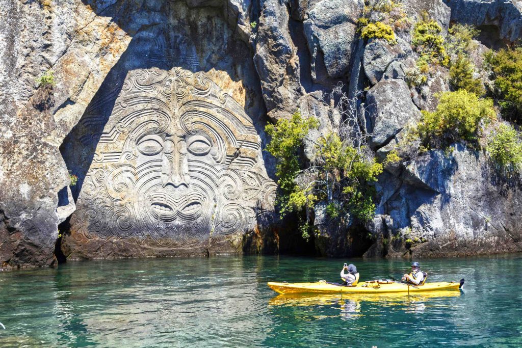 New Zealand, view to Maori cave art with two tourists in kayak in front