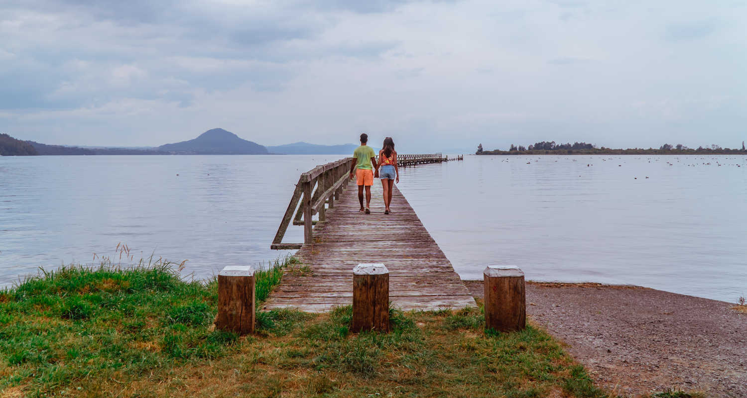 Couple on wooden brown jetty on calm relaxing Lake Taupo, North Island, New Zealand, NZ