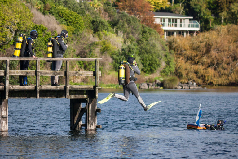 Divers jumping off wooden jetty on lake Pupuke, New Zealand