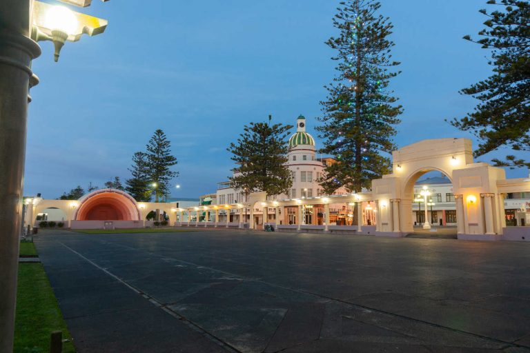 Marine Parade Sound Shell with colonnade, Norfolk Pines and city deco style buildings behind, Napier, New Zealand