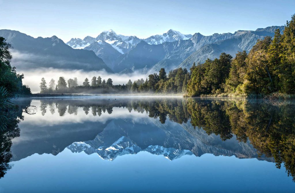 Matheson Lake New Zealand on a still morning with mist rising and Mount Cook in the background