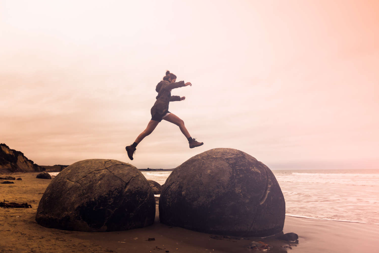 Woman jumping on Moeraki Boulders, South Island New Zealand